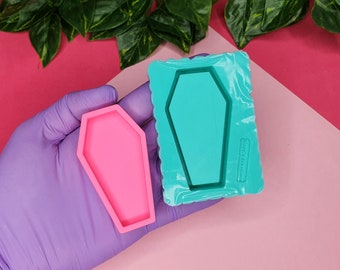 May include: Two silicone moulds for making resin crafts. One mould is pink and the other is teal. Both moulds are shaped like a coffin.