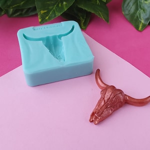 以下が含まれることがあります： 樹脂製の雄牛の頭蓋骨を作るためのシリコンモールドと、その横に銅色の樹脂製の雄牛の頭蓋骨があります。