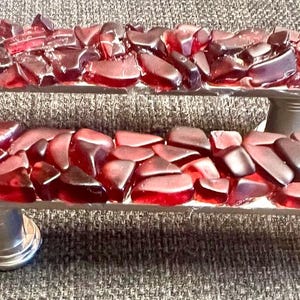 May include: Two door handles made from red glass mosaic with silver metal bases. The handles are made of small, irregular pieces of red glass.