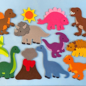 May include: A collection of colorful felt dinosaur cutouts, including a brown T-Rex, a pink Stegosaurus, and a blue Brontosaurus, arranged on a light blue background. Also includes a felt sun and volcano.