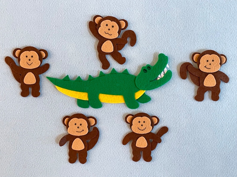 May include: Five felt animal figures, including a green and yellow alligator and four brown monkeys. The monkeys have brown fur, white faces, and black eyes. The alligator has a toothy grin.