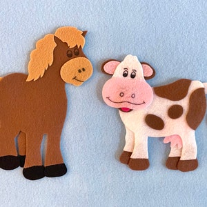May include: A brown felt horse with a light brown mane and a white felt cow with brown spots. Both animals are smiling.