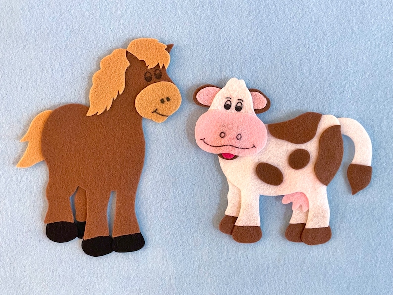 May include: A brown felt horse with a light brown mane and a white felt cow with brown spots. Both animals are smiling.