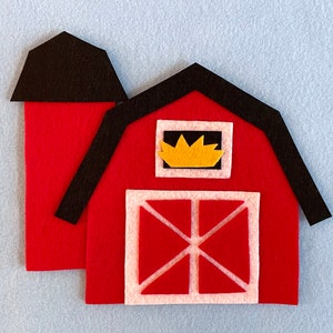 May include: A red felt barn with a black roof and a yellow window. The barn has a white door with a red X.