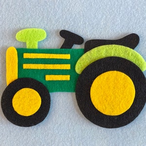 May include: A green felt toy tractor with yellow wheels and a black exhaust pipe. The tractor has a green and yellow striped body.