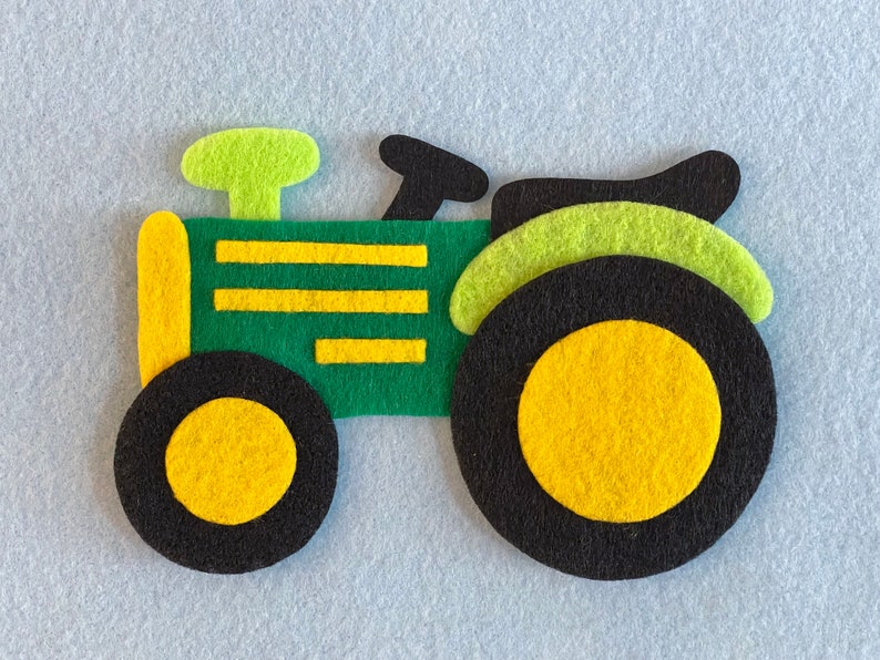 May include: A green felt toy tractor with yellow wheels and a black exhaust pipe. The tractor has a green and yellow striped body.