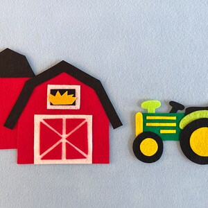 May include: A red felt barn with a black roof and a yellow window. A green felt tractor with black wheels and yellow tires is next to the barn.