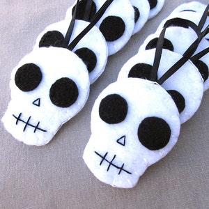 May include: A set of white felt skull ornaments with black felt eyes and mouths. The skulls are strung together with black ribbon.