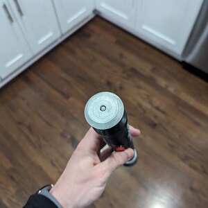 May include: A black and silver lightsaber with a red button. The lightsaber has a circular, silver cap on the end.