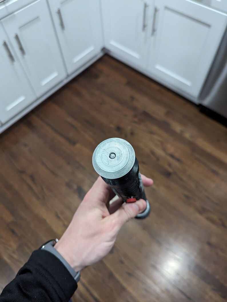 May include: A black and silver lightsaber with a red button. The lightsaber has a circular, silver cap on the end.