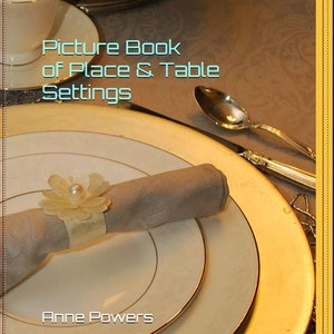 May include: A picture book titled "Picture Book of Place & Table Settings" by Anne Powers. The cover features a close-up of a white dinner plate with a gold rim, a napkin, and a napkin ring.