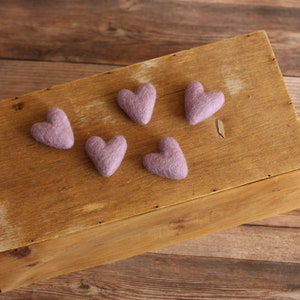 Puede incluir: Cinco pequeños corazones de fieltro de color morado claro están dispuestos en una caja de madera. La caja es de madera marrón claro y tiene un acabado natural.