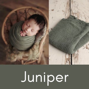 May include: A soft, sage green newborn photography backdrop. The backdrop is made of a textured fabric and is folded in half. The backdrop is on a white wooden surface. Juniper.
