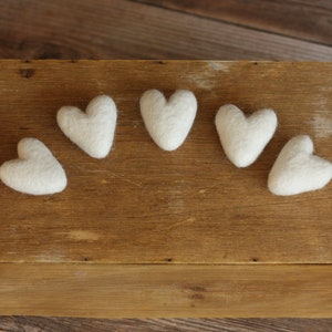 Puede incluir: Cinco corazones de fieltro blanco dispuestos en arco sobre una superficie de madera.