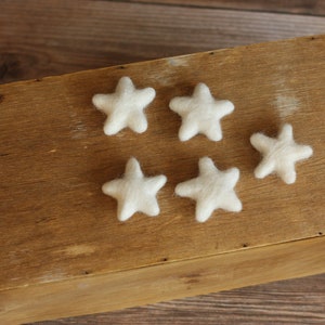Puede incluir: Seis estrellas de fieltro blanco sobre una superficie de madera. Las estrellas están dispuestas en semicírculo.