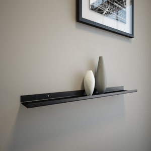 May include: A black metal shelf mounted on a wall with two vases on top. The vase on the left is white and the vase on the right is gray.