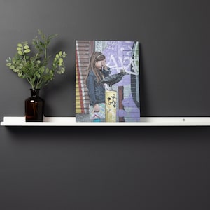 May include: A white shelf with a brown glass vase holding a green plant and a framed print of a girl with a black bird on her shoulder. The print is set against a colorful graffiti background.