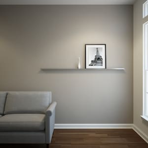 May include: A modern living room scene featuring a gray sofa, a floating shelf, and a framed black and white photograph of the Eiffel Tower. A small white vase sits on the shelf. The room has hardwood floors and neutral-toned walls.