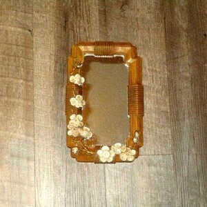 May include: A rectangular wall mirror featuring a brown wooden frame with ribbed detailing at the top, bottom, and sides. The frame is decorated with a cluster of light-colored, five-petaled floral accents that extend along the left and bottom edges.