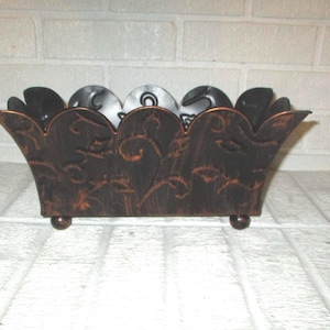 May include: A rectangular metal planter with a dark brown finish and copper-colored highlights. The container features a scalloped top edge, intricate embossed vine patterns on the sides, and stands on four small, rounded ball-shaped feet.