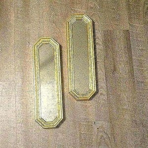 May include: Two vintage rectangular mirrors with gold frames. The mirrors have an octagonal shape and are placed on a wooden surface. The frames have a decorative pattern.