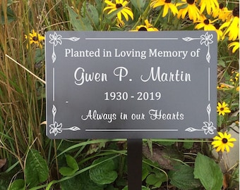May include: A black metal garden memorial plaque with white text that reads "Planted in Loving Memory of Gwen P. Martin 1930-2019 Always in our Hearts". The plaque is attached to a black metal stake.