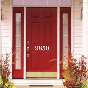 Pode incluir: Uma porta de entrada vermelha com uma placa de porta de lat&atilde;o e um n&uacute;mero de casa branco "9850" na porta. A porta tem uma janela de vidro de cada lado e uma pequena janela de vidro acima da porta.