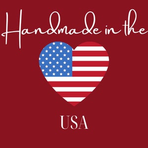 May include: A red background with the text "Handmade in the USA" in white script. A heart-shaped design features the American flag, with blue stars and red and white stripes.