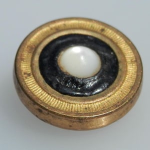 May include: A gold-colored button with a black ring around a white pearl-like center.