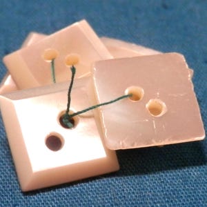 May include: Four pink buttons with two holes each, threaded with green string.