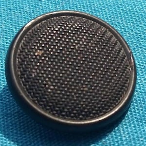 Könnte beinhalten: Ein schwarzer Knopf mit einem strukturierten, kreisförmigen Design. Der Knopf hat eine erhabene, kreisförmige Mitte und einen glatten, abgerundeten Rand.