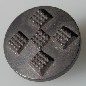 Könnte beinhalten: Ein schwarzer Metallknopf mit einem kreuzförmigen Design. Das Kreuz besteht aus vier Quadraten, die jeweils ein Gittermuster aufweisen.