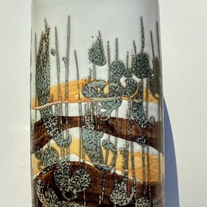 Puede incluir: Un jarrón cilíndrico de cerámica con fondo blanco y diseño en capas. El diseño presenta bandas horizontales marrones, amarillas y blancas, con formas verticales y orgánicas en tonos marrones y grises.