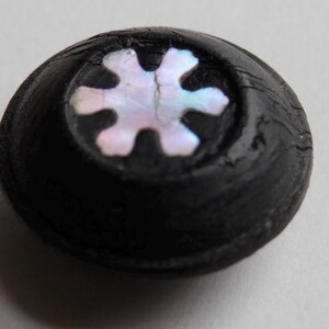 Könnte beinhalten: Ein schwarzer Knopf mit einem weißen, schimmernden Schneeflocken-Design.