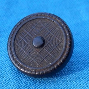 Könnte beinhalten: Ein schwarzer Knopf mit einem erhabenen, kreisförmigen Design. Der Knopf hat ein konzentrisches Kreisdesign mit einem kleineren, erhabenen Kreis in der Mitte.