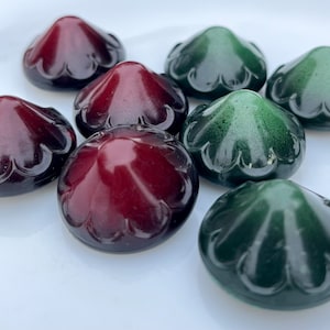 Puede incluir: Ocho botones decorativos de vidrio en dos colores: burdeos y verde oscuro. Los botones tienen forma de cúpula con un borde festoneado.