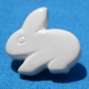 May include: A white ceramic bunny figurine. The bunny is in a seated position with its ears upright. The figurine is smooth and glossy, with a simple, minimalist design. The background is a solid blue.