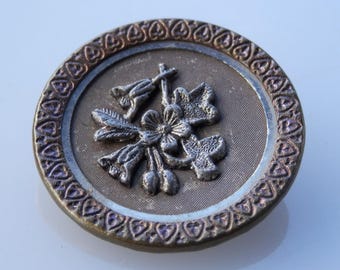 May include: A silver metal button with a raised design of a flower and leaves. The button has a decorative border of hearts.