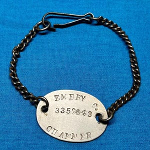 以下が含まれることがあります： 留め具付きの銀色のチェーンに、"EMERY 3359043 Co. CHAFFEE"と刻まれた銀色の楕円形のドッグタグ