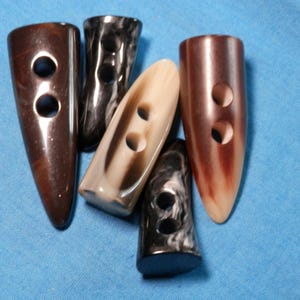 May include: Five different types of brown, black, and white plastic buttons with two holes each. The buttons are shaped like a teardrop and have a smooth, glossy finish.