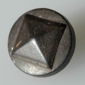 Könnte beinhalten: Ein schwarzer Metallknopf mit einem erhabenen, quadratischen Pyramidenmuster.