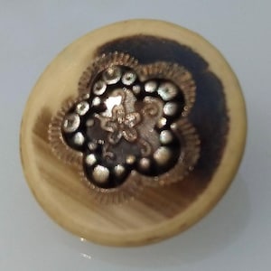 Könnte beinhalten: Ein runder, hölzerner Knopf mit einem braunen und schwarzen Blumendesign. Das Design zeigt eine Blume mit einem Zentrum, das aus einem braunen und schwarzen Wirbel besteht.