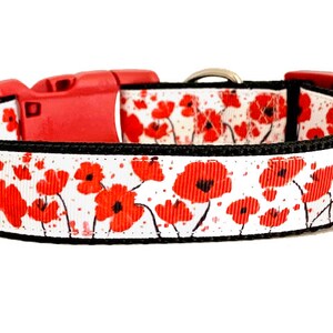 May include: White dog collar with a red poppy floral print. The collar has a black trim and a red plastic buckle.