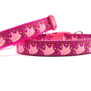 May include: Two pink dog collars featuring a repeating pattern of light pink crowns and gold dots on a magenta background. The collars have pink plastic buckles, designed for pets.