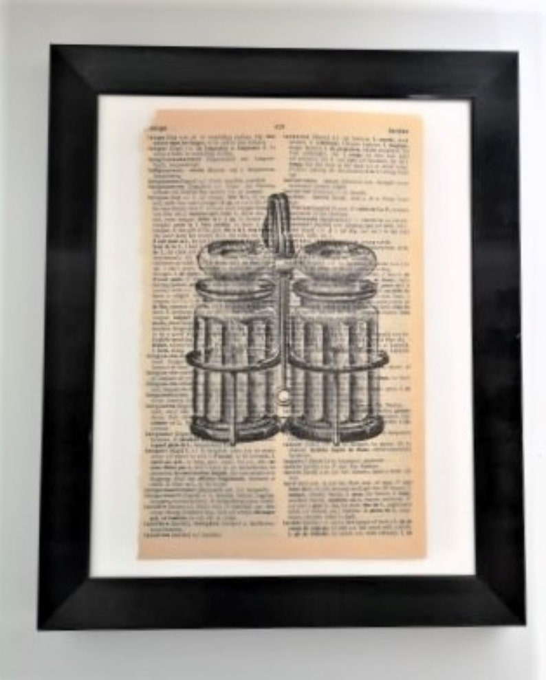 May include: A framed wall art piece featuring a black ink illustration of a double-chambered glass oil and vinegar cruet set printed directly onto a vintage dictionary page with aged, tan-colored paper and visible columns of printed text.