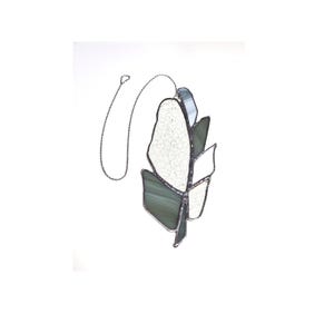 May include: A stained glass feather ornament featuring a combination of textured white glass and smooth, translucent sage green glass pieces. The segments are joined by dark metal solder lines, and the piece hangs from a thin silver-toned metal chain.