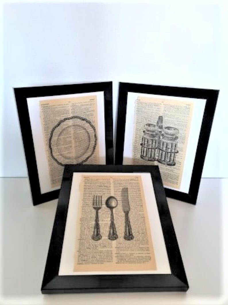 May include: Three framed art prints featuring black ink illustrations on vintage dictionary pages. One print shows a dinner plate, another displays salt and pepper shakers, and the third depicts a fork, spoon, and knife set in black frames.