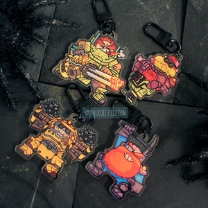 May include: Four acrylic keychains with cartoon characters in yellow, red, blue, and brown. Each character has black outlines and is in a different pose. The keychains have black clasps. The website vaahlkult.etsy.com is visible.
