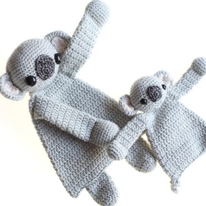 May include: Two crocheted koala plushies, one larger than the other, in a light gray color. Both have black eyes and a brown nose.