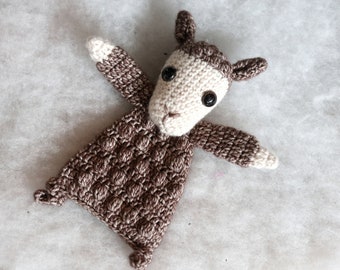 May include: A brown and white crocheted stuffed animal shaped like a lamb. The lamb has black eyes and a white face.